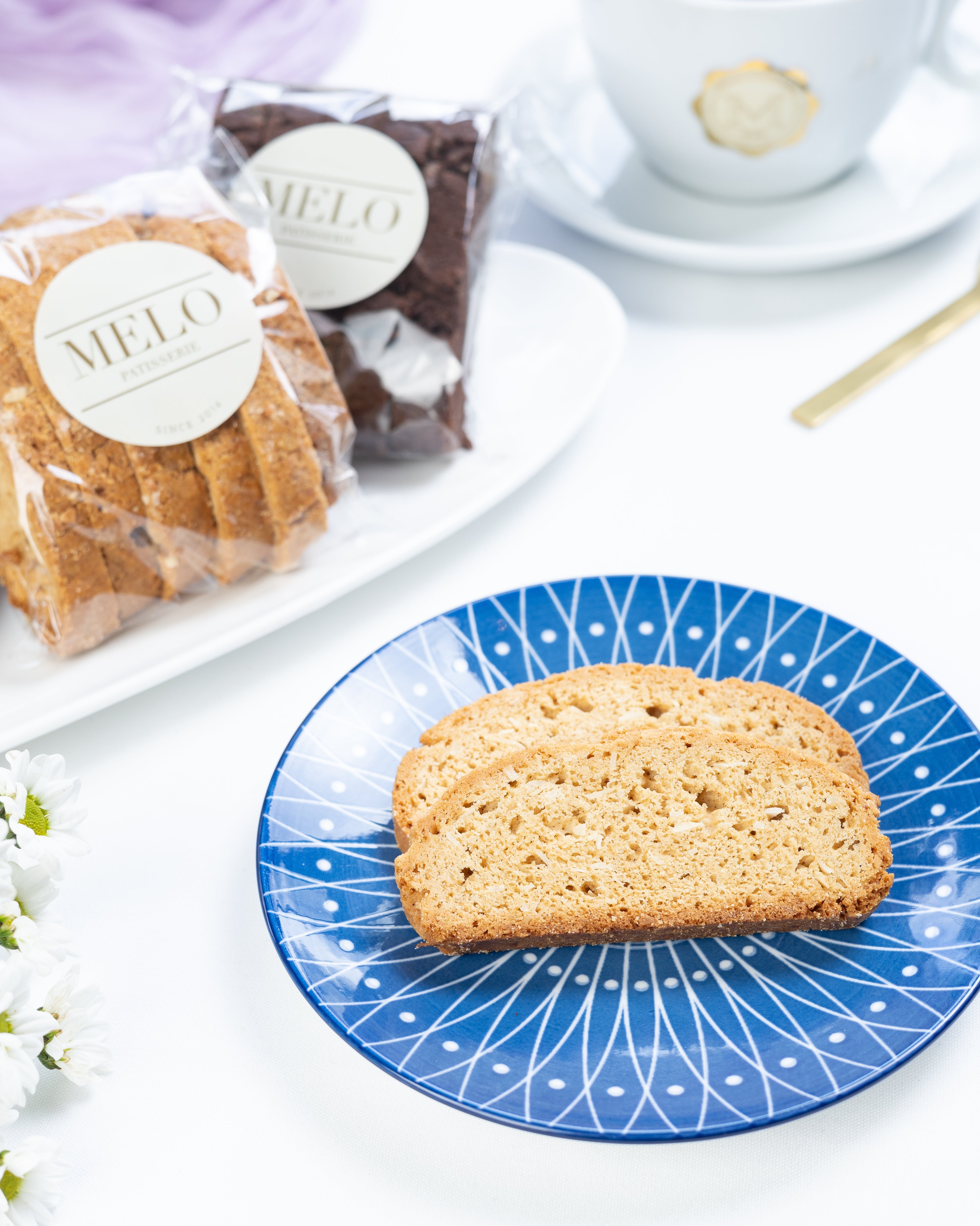 Biscotti on a blue plate with a cup of coffee and packaged pastries in the background.