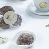 Almond Earl Grey cookies in a white dish with a cup of coffee and packaging labeled 'Melo' in the background.