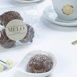 Almond earl grey cookies in a white dish with a cup of coffee and packaging labeled 'Melo' in the background.