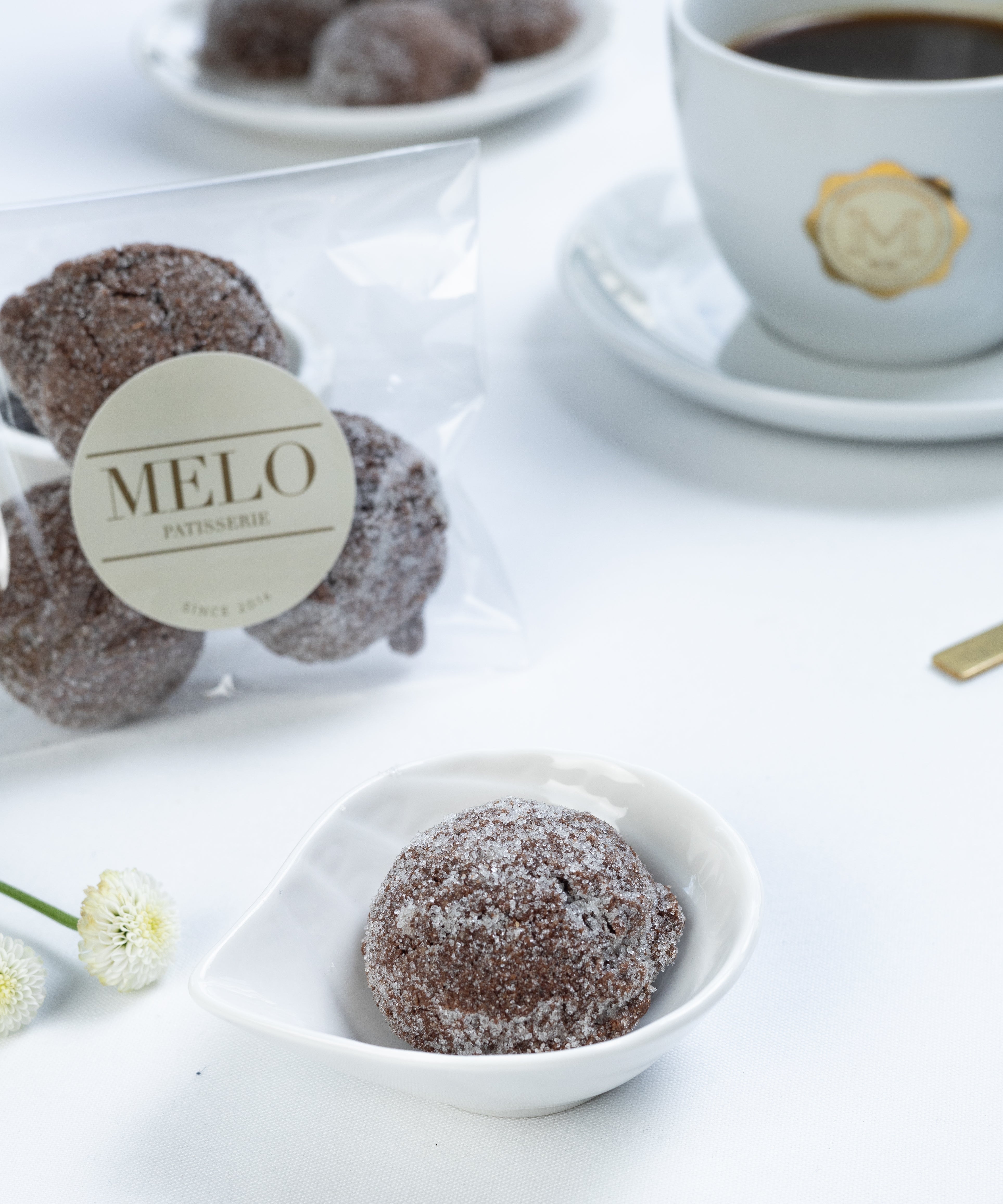 Almond earl grey cookies in a white dish with a cup of coffee and packaging labeled 'Melo' in the background.
