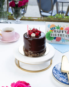 Chocolate cake with red berries on a white table with pink roses and a birthday card.