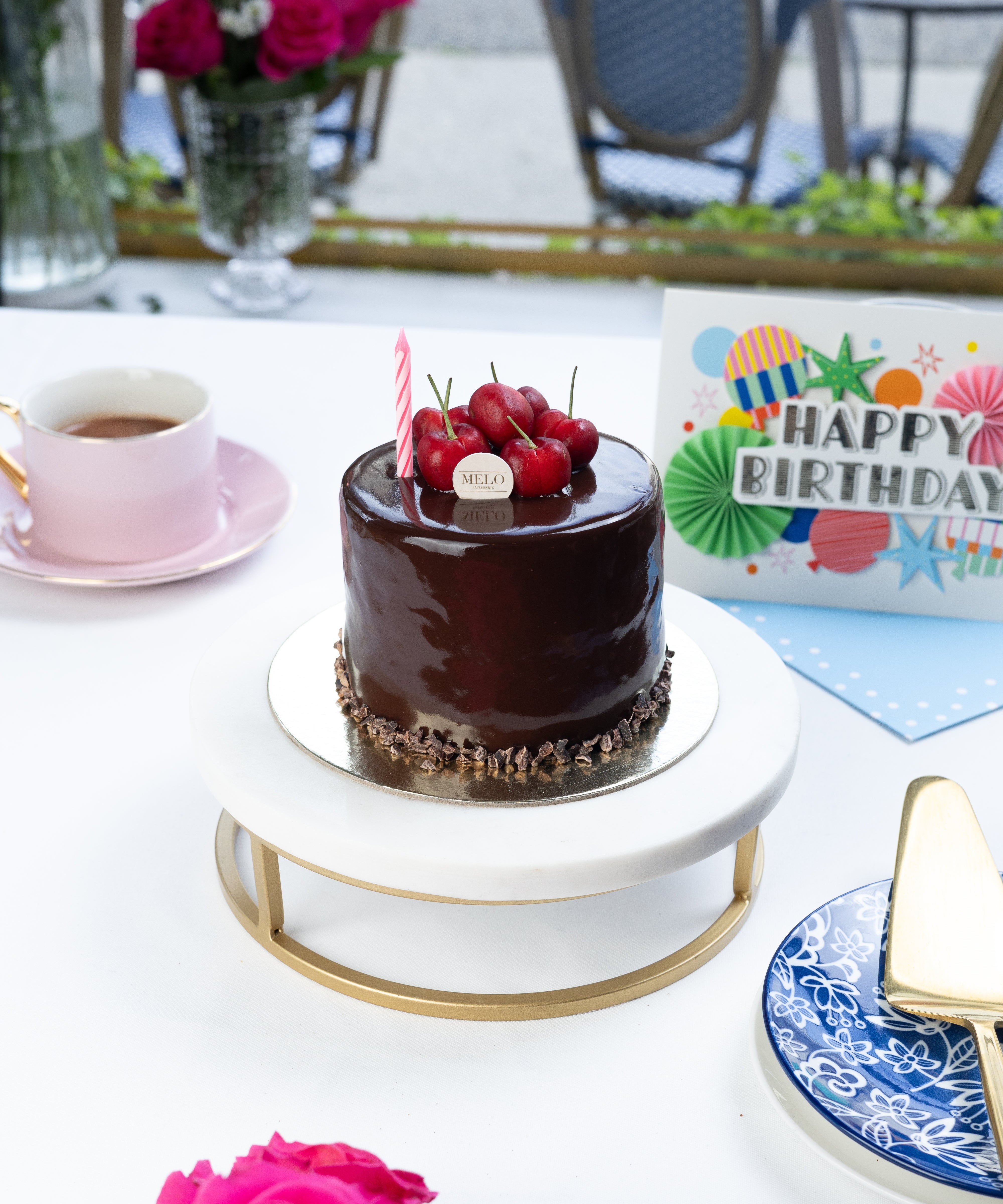 Chocolate cake with red berries on a white table with pink roses and a birthday card.