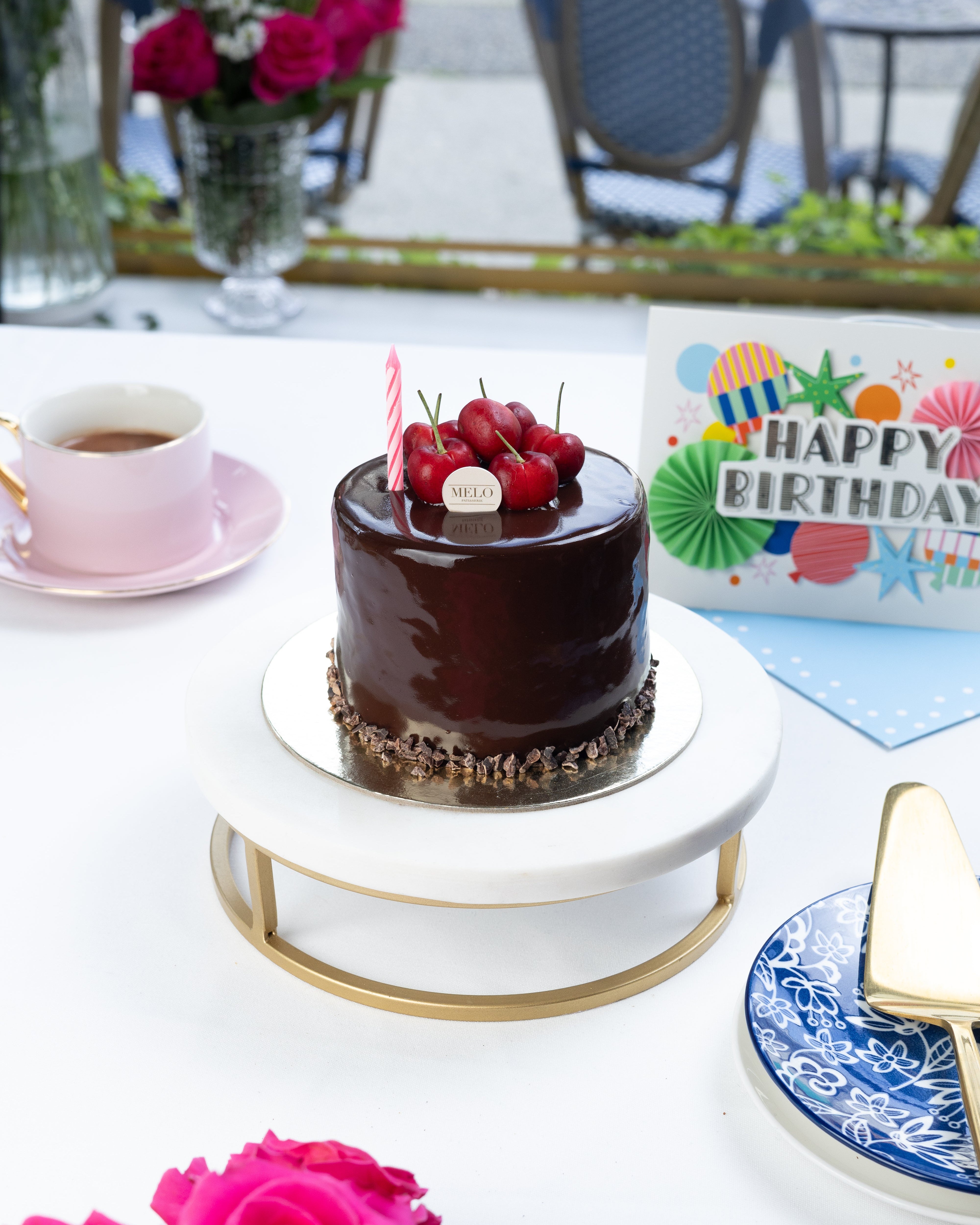 Chocolate cake with red berries on a white table with pink roses and a birthday card.