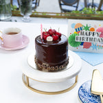 Chocolate cake with red berries on a white table with pink roses and a birthday card.