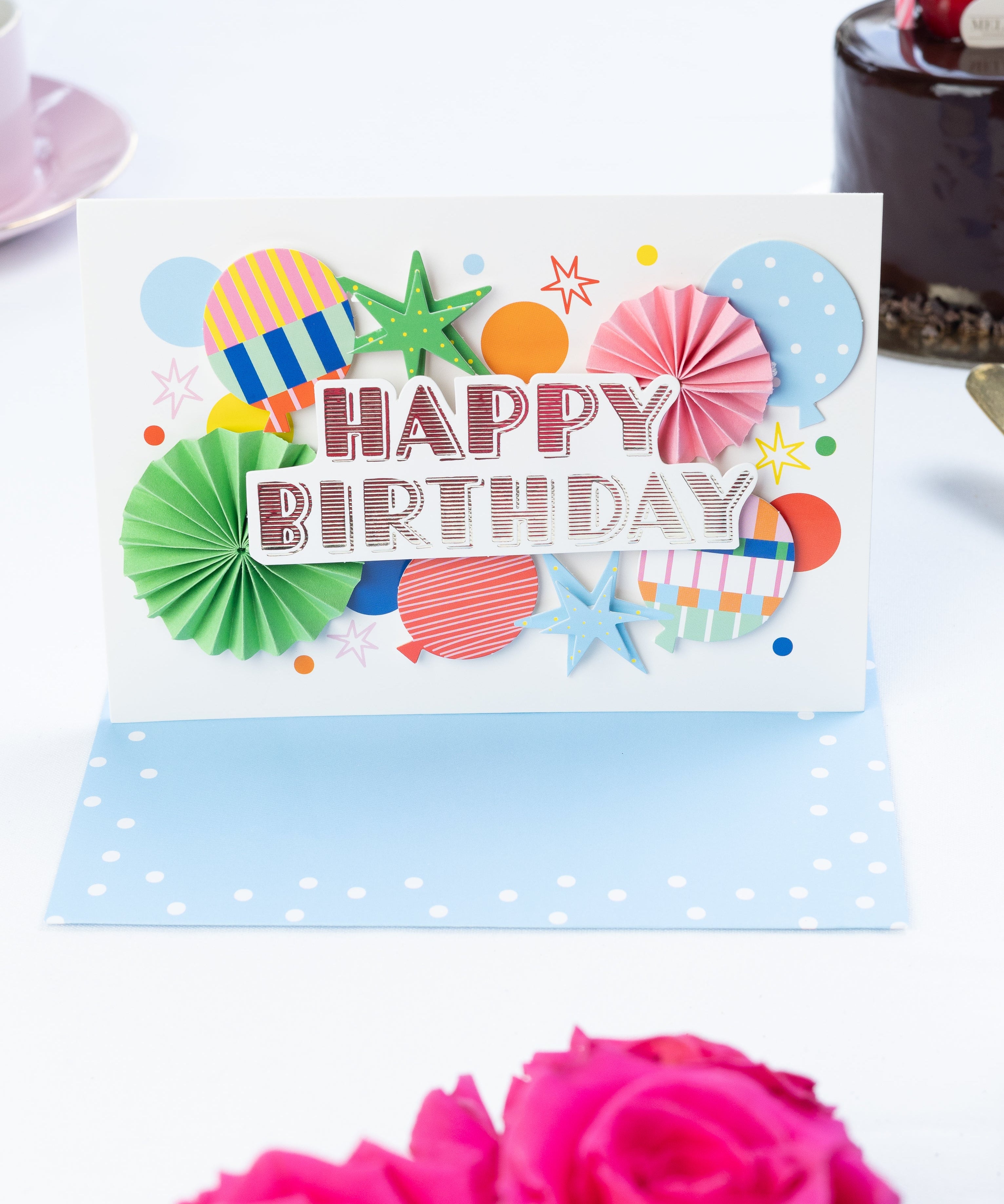 Colorful birthday card with decorative elements on a white surface with pink roses.