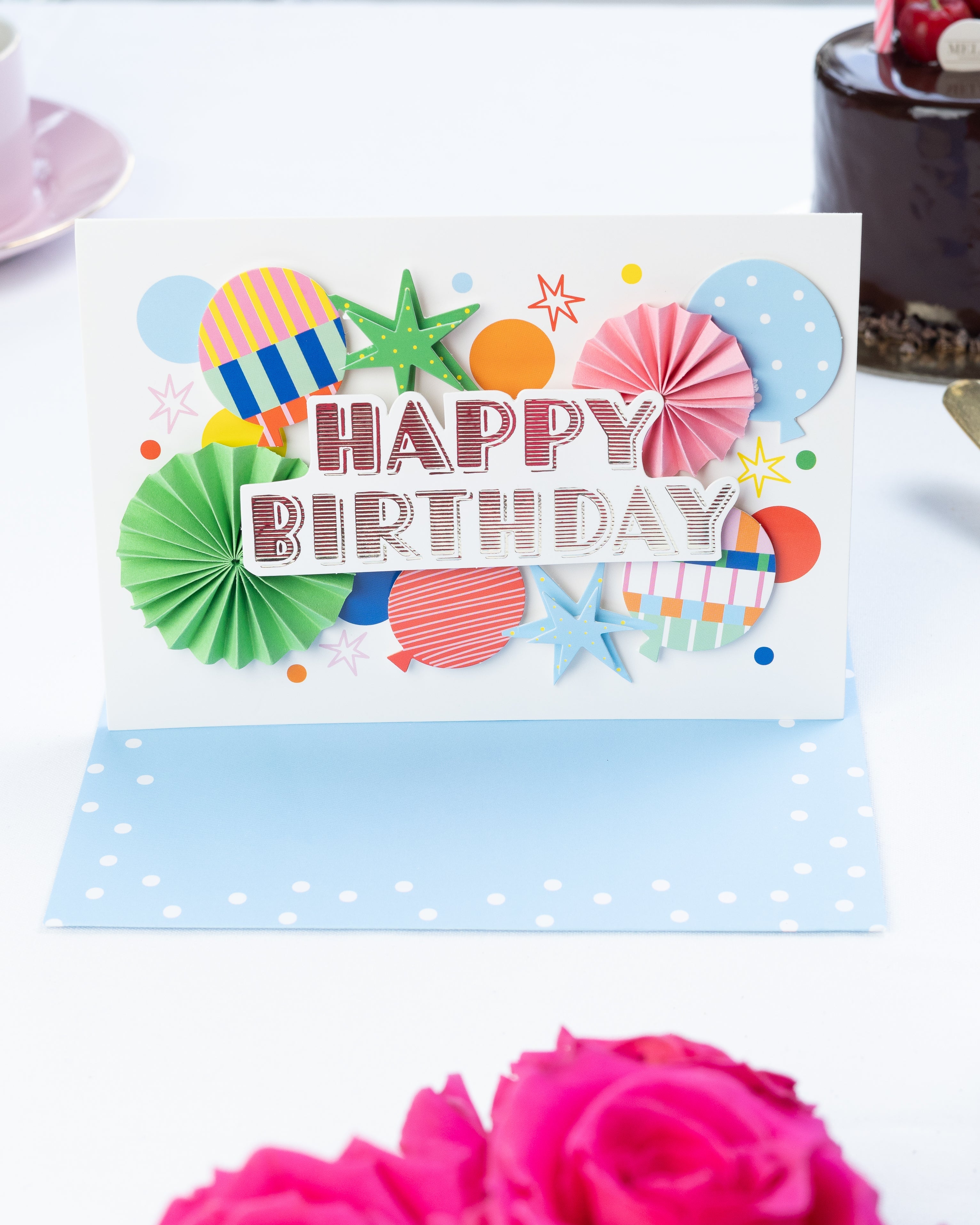 Colorful birthday card with decorative elements on a white surface with pink roses.