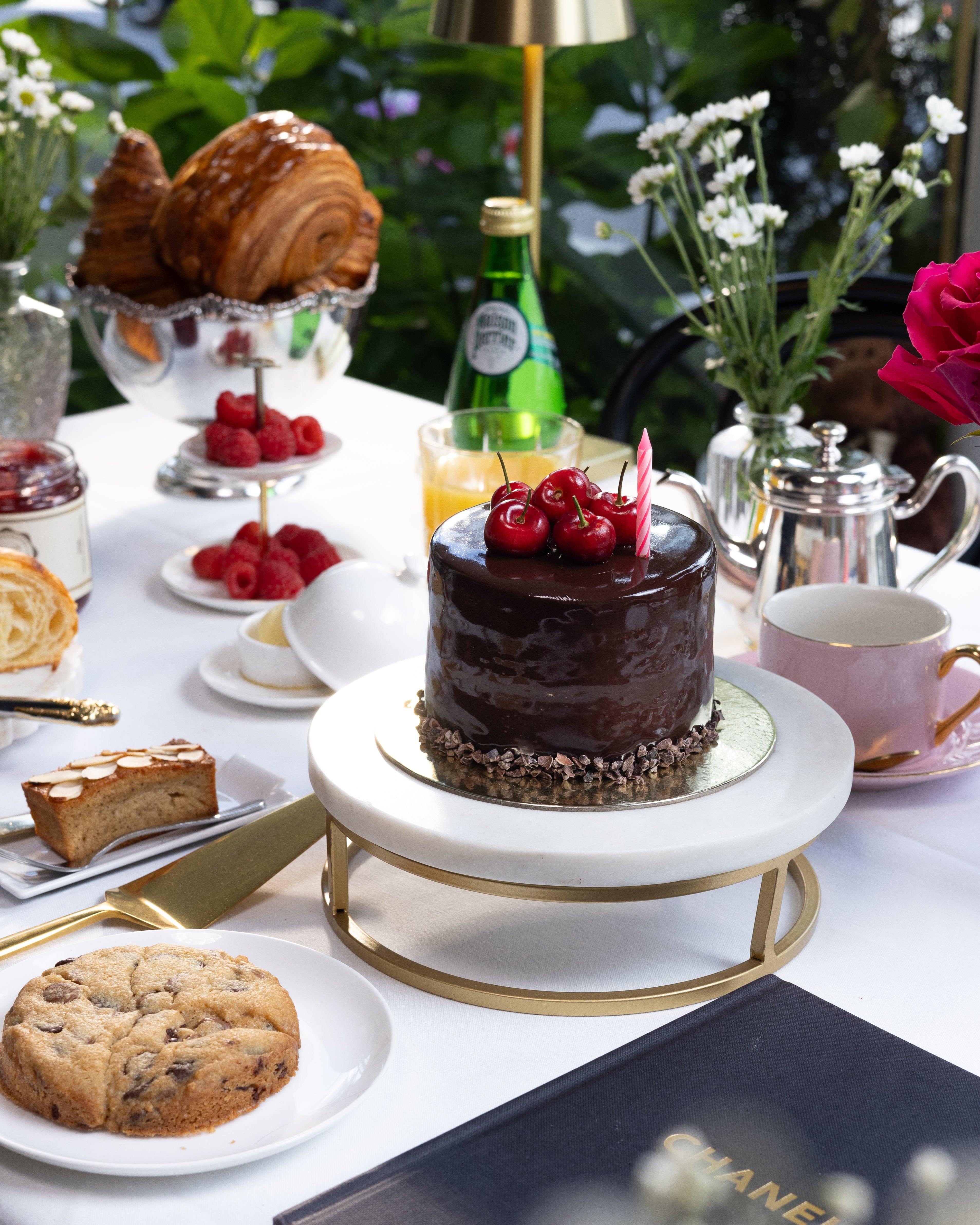 Table setting with a chocolate cake, cookies, and a Chanel menu in an outdoor setting.